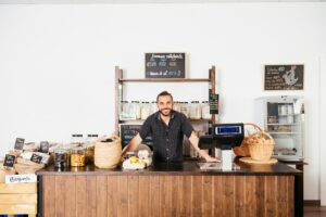 Smiling Storekeeper Behind Wooden Counter in a Modern Grocery Store During Business Hours